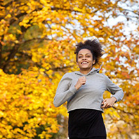 Woman jogging with yellow fall leaves in the background.