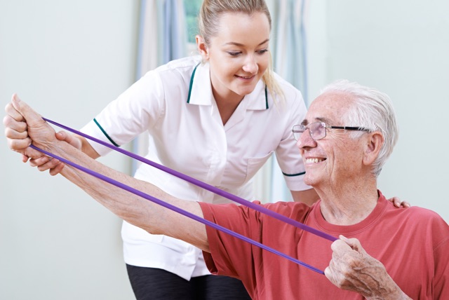 Female PT helping an older man with an exercise band.