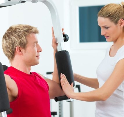 woman helping man use a piece of workout equipment.