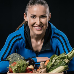 female athlete smiling behind a pile of vegetables.