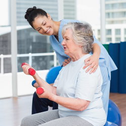 A female physical therapist helping elderly woman lift weights.