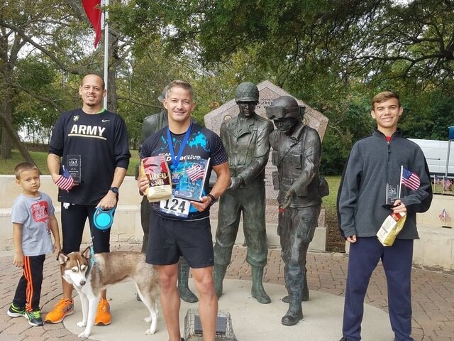 Dan standing holding awards near veteran statues.