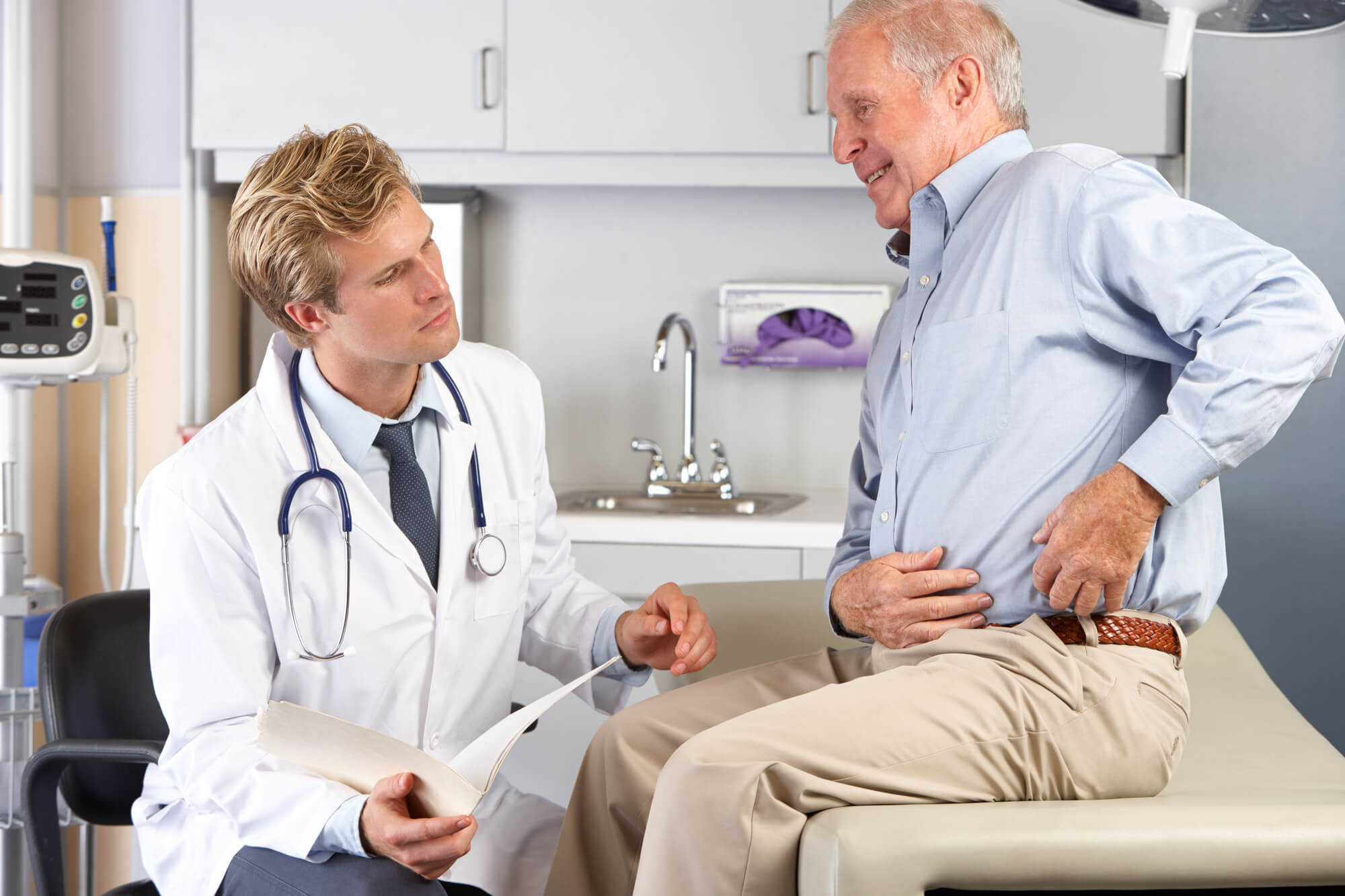 Older man points to his hip while talking with Doctor.