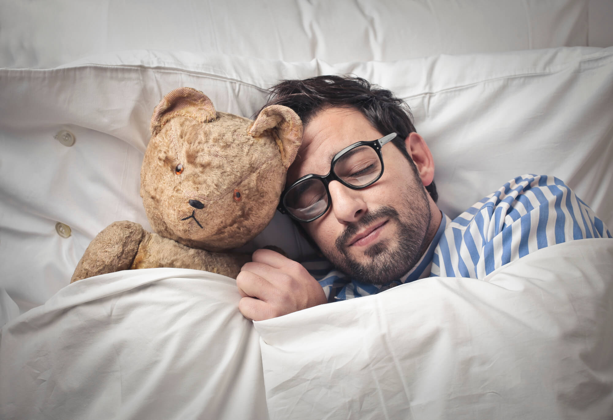 Adult man snuggling teddy bear, sleeping in bed.