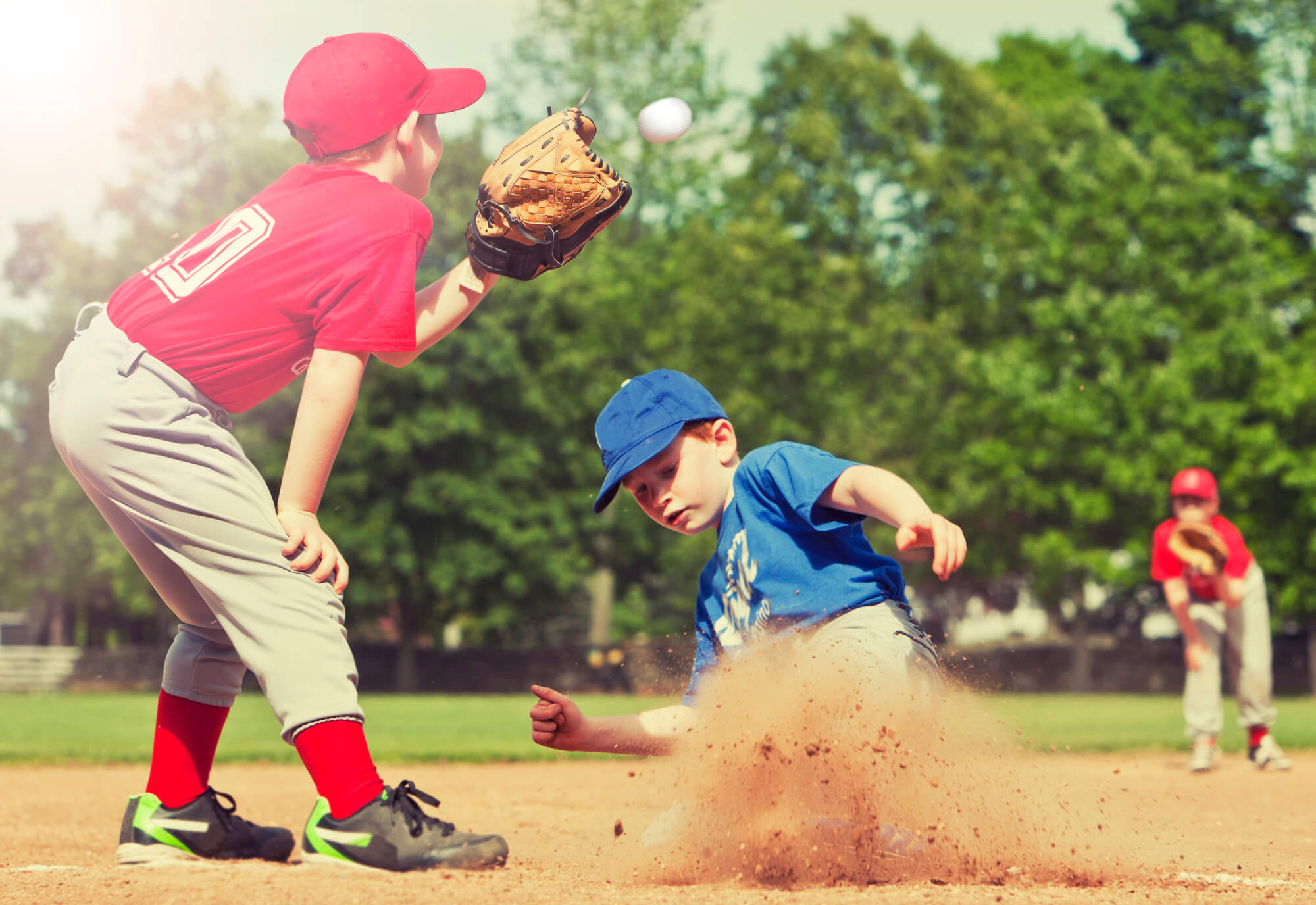 Little league baseball player sliding into second base.