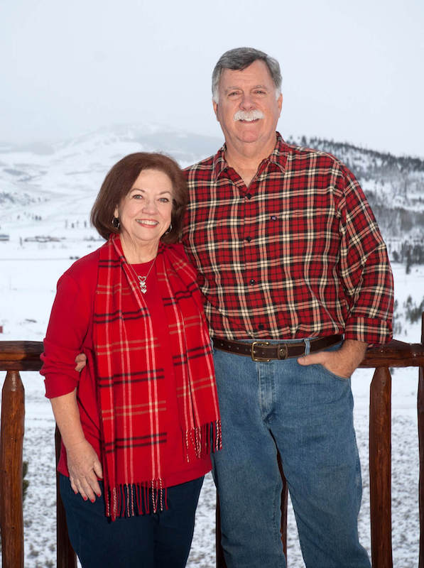 Charles and his partner smiling outside with a snowy mountain in the background.