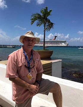 Maurice smiling in a Hawaiian shirt near a warm coast.