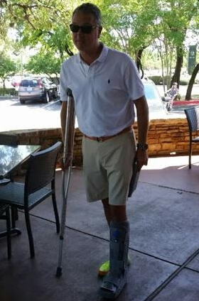 Christoper standing with a brace on his lower leg and a crutch on the patio at a restaurant.