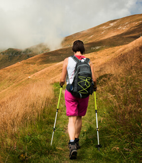 Woman backpacking along a treeless hillside with walking stick.