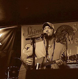 Sepia colored shot of Joshua playing guitar at a show.