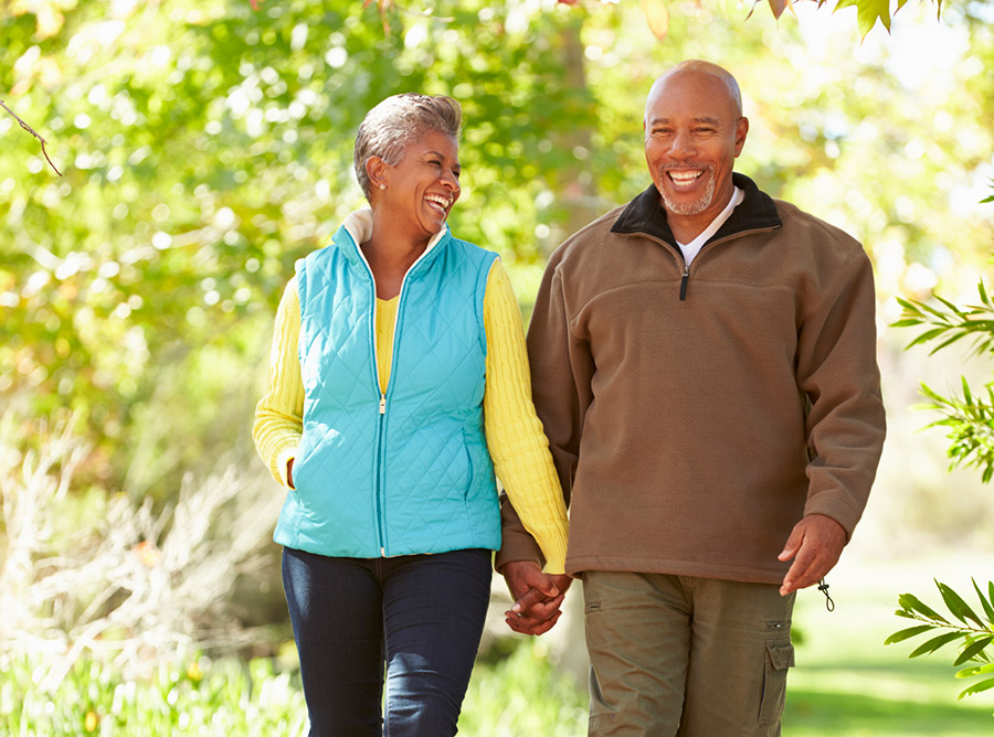 Older couple smiling, walking through the park.