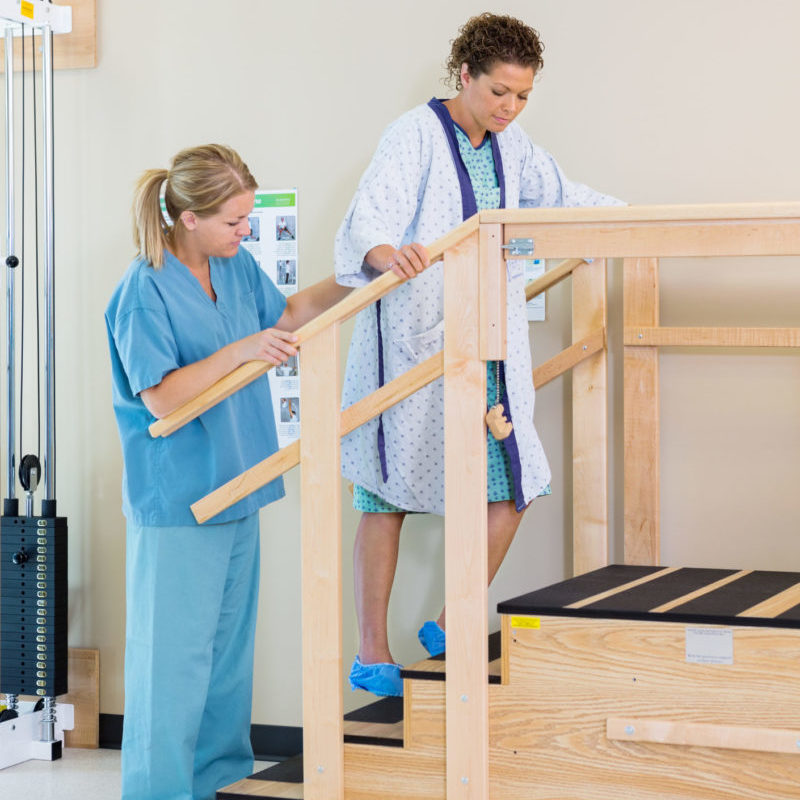 Physical therapist rehabilitating woman by walking up stairs.