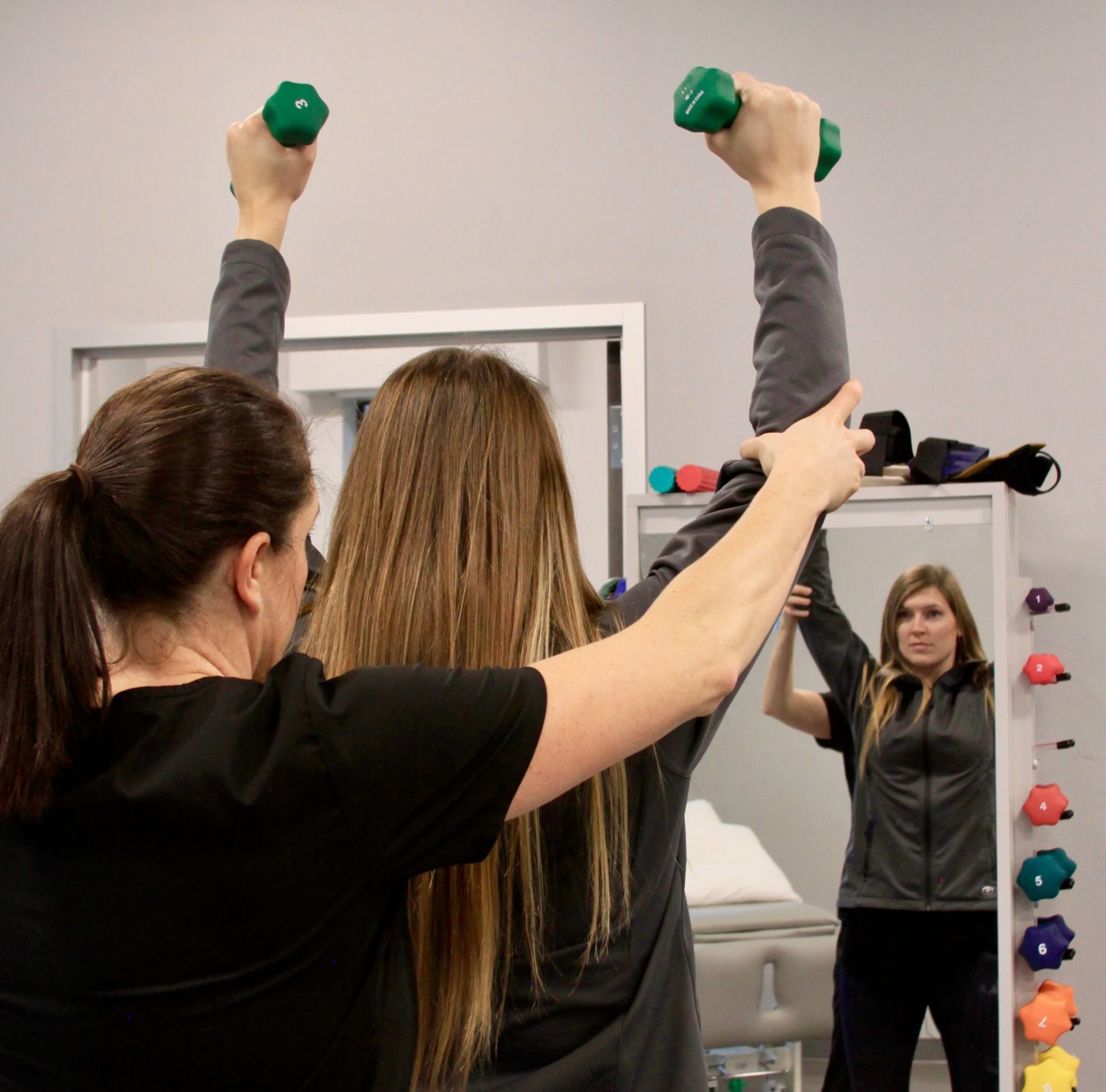 Physical therapist assisting young woman with weights during therapy.